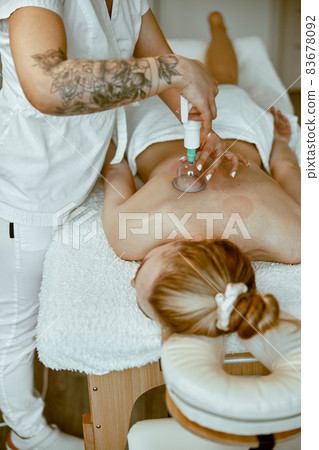 professional female specialist is doing cupping therapy on the back of beautiful caucasian lady professional female specialist is doing cupping therapy on the back of beautiful caucasian lady 83678092
