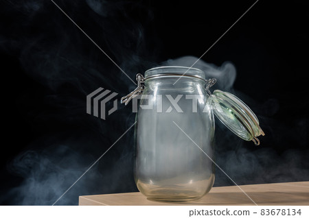 Glass jar with a lid filled with smoke on a black background. Fog in a transparent container on the table. Glass jar with a lid filled with smoke on a black background. Fog in a transparent container on the table. 83678134