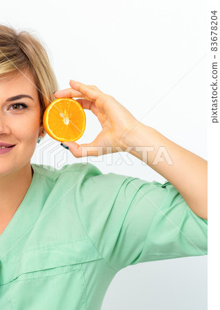 Portrait of young smiling blonde woman cosmetologist with halves of oranges on white background. Portrait of young smiling blonde woman cosmetologist with halves of oranges on white background. 83678204