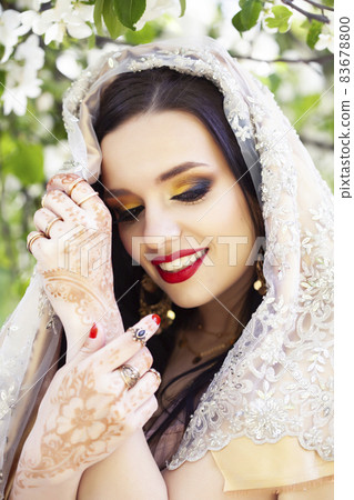 young pretty indian girl in jewelry and veil posing cheerful happy smiling in green park, lifestyle people concept 83678800