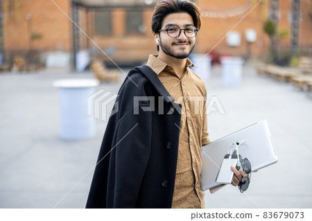 Indian man with gadgets looking at camera outdoors Indian man with gadgets looking at camera outdoors 83679073