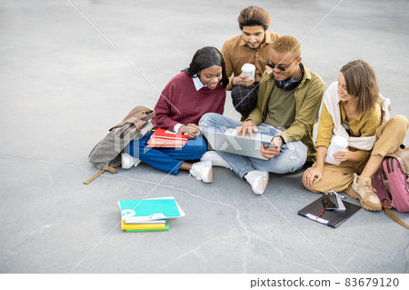 Students watching something on laptop on asphalt Students watching something on laptop on asphalt 83679120