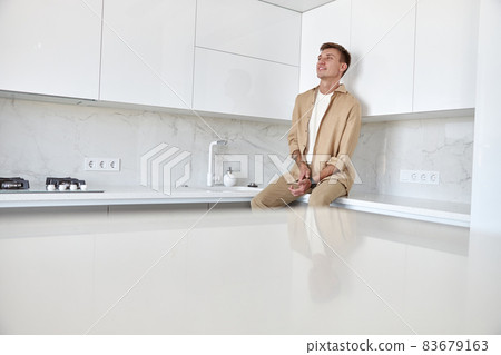 Happy handsome man is standing on minimalistic kitchen and smiling 83679163