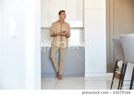 Hadsome smiling man is chilling on the minimalistic kitchen with smartphone 83679166