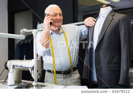 Professional tailor communicates with the client on mobile phone and takes notes in notebook Professional tailor communicates with the client on mobile phone and takes notes in notebook 83679522