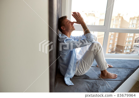 Happy adult caucasian male is sitting near panoramic window and chilling 83679964