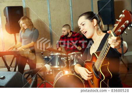 Attractive female soloist playing guitar and singing with her mu 83680528