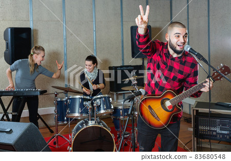 Guy guitar player and singer practicing with band members in recording studio Guy guitar player and singer practicing with band members in recording studio 83680548