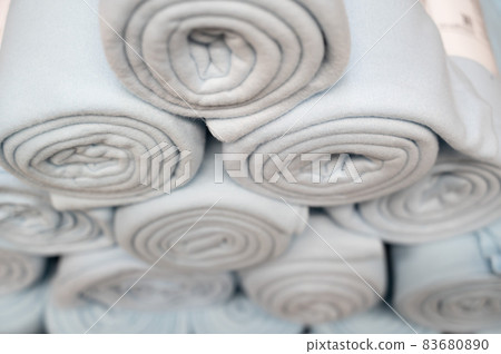 A stack of knitted white plaid folded into a roll. Several handmade woolen texture blanket in stock. A stack of knitted white plaid folded into a roll. Several handmade woolen texture blanket in stock. 83680890