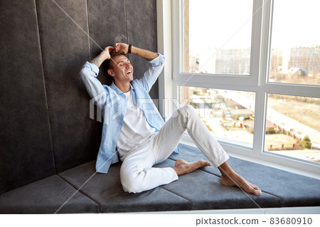 Happy adult caucasian male is sitting near panoramic window and chilling Happy adult caucasian male is sitting near panoramic window and chilling 83680910