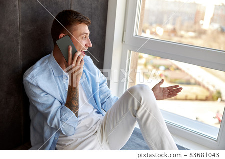 Happy adult caucasian male is sitting near panoramic window and chilling Happy adult caucasian male is sitting near panoramic window and chilling 83681043