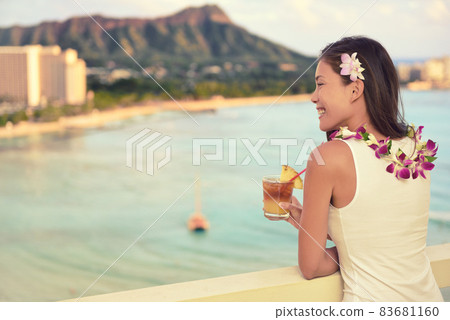 Hawaii vacation summer travel- Mai Tai and aloha spirit. Asian woman relaxing drinking Hawaiian cocktail drink Mai Tai, at sunset view of Waikiki beach in Honolulu, Oahu, USA travel. 83681160