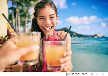 Cocktail toast couple going out on beach restaurant cheering with rum mai tai drinks on Waikiki, Honolulu, Hawaii travel. Happy Asian woman holding glass of alcohol toasting with man. 83681162