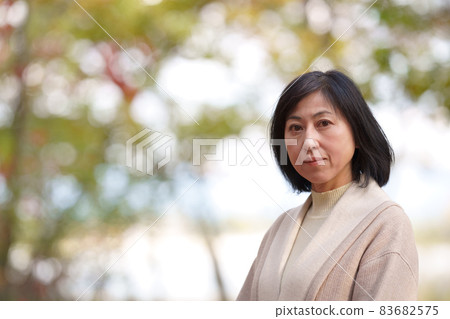 A lonely middle-aged woman looking at the camera in an autumn park A lonely middle-aged woman looking at the camera in an autumn park 83682575