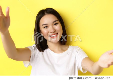 Close up of modern asian girl taking selfie on smartphone, mobile camera view of pretty woman smiling, standing over yellow background Close up of modern asian girl taking selfie on smartphone, mobile camera view of pretty woman smiling, standing over yellow background 83683046