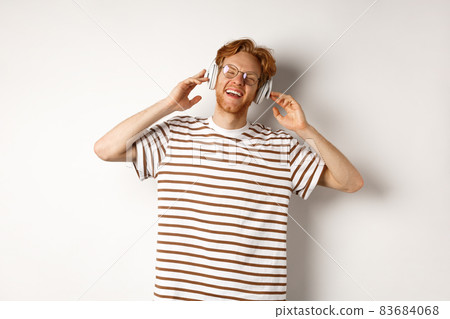 Technology concept. Happy redhead man listening music in headphones and singing along, standing over white background 83684068