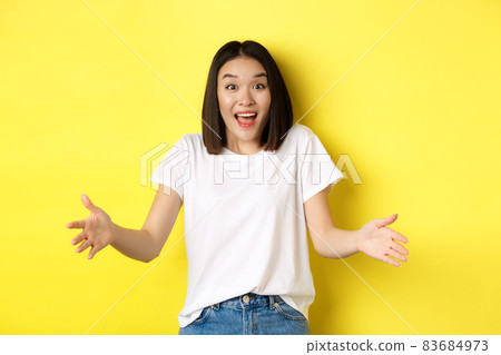 Excited young asian woman spread out hands as if holding large, big object, showing size and look amazed, standing over yellow background Excited young asian woman spread out hands as if holding large, big object, showing size and look amazed, standing over yellow background 83684973