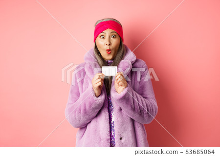 Shopping and fashion concept. Image of amazed asian senior woman checking out promo offer, holding plastic credit card and stare impressed at camera, pink background Shopping and fashion concept. Image of amazed asian senior woman checking out promo offer, holding plastic credit card and stare impressed at camera, pink background 83685064