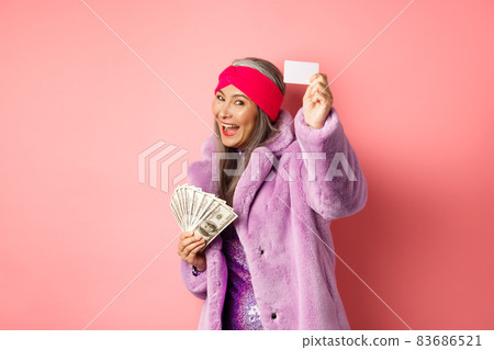 Shopping and fashion concept. Fashionable funky asian woman showing plastic credit card, paying contactless, holding money in other hand, pink background Shopping and fashion concept. Fashionable funky asian woman showing plastic credit card, paying contactless, holding money in other hand, pink background 83686521