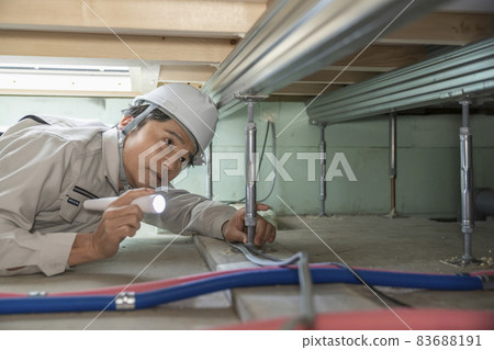A man in work clothes inspecting the underfloor of a house A man in work clothes inspecting the underfloor of a house 83688191
