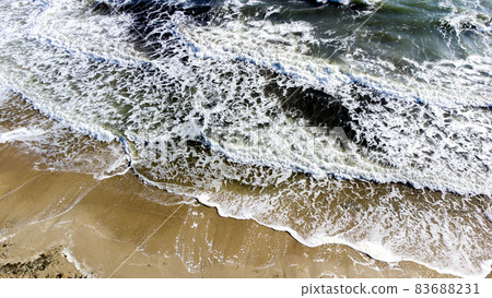 Aerial drone view flight over sea waves that roll onto sandy shore. Aerial drone view flight over sea waves that roll onto sandy shore. 83688231