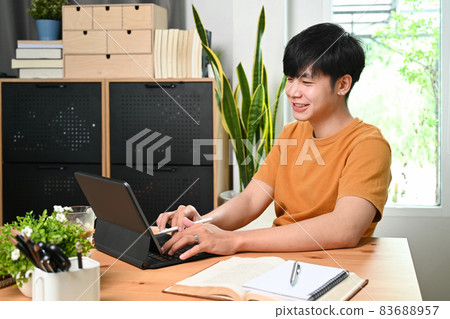 Smiling asian man in casual clothes browsing internet with computer tablet at home. Smiling asian man in casual clothes browsing internet with computer tablet at home. 83688957