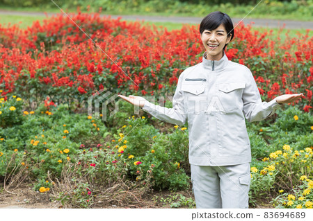 A woman wearing work clothes and standing in front of the flowerbed A woman wearing work clothes and standing in front of the flowerbed 83694689