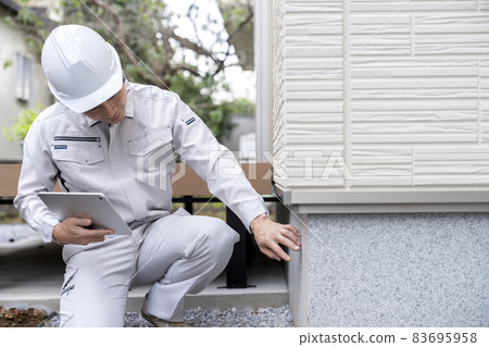 A man in work clothes inspecting the foundation of a house A man in work clothes inspecting the foundation of a house 83695958