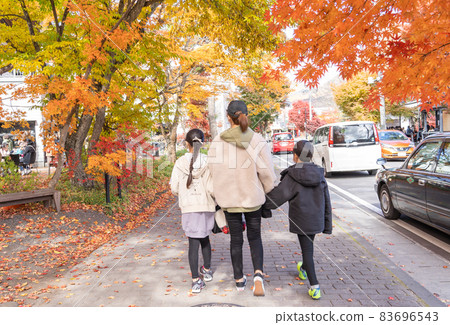 A family of three strolling through the autumn leaves 83696543