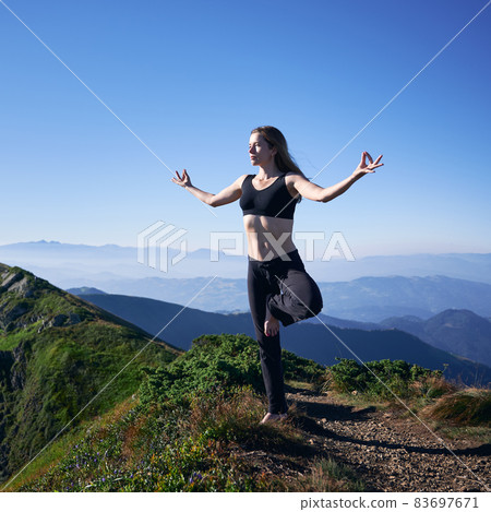 Full length of fit woman in sportswear balancing on one leg and doing Gyan mudra hand gesture while practicing yoga outdoors. Athletic young woman doing yoga exercise in mountains. Full length of fit woman in sportswear balancing on one leg and doing Gyan mudra hand gesture while practicing yoga outdoors. Athletic young woman doing yoga exercise in mountains. 83697671