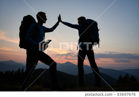Full length of young man and woman travelers giving high five while hiking together in the mountains during sunset. Concept of travelling, hiking and relationships. 83697676