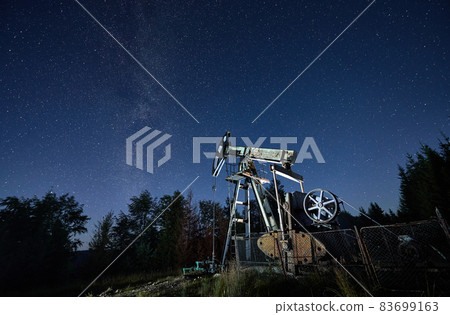 Equipment for oil and gas production. Classical rod pump using in the oil industry to pump oil from wells. Pumping natural fuel at night under starry sky and magical Milky Way galaxy. 83699163