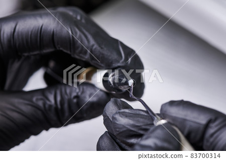 Close up of doctor hands in black sterile gloves preparing bracket bonding paste. Specialist holding dental instrument and adhesive paste for braces placement. Concept of orthodontic treatment 83700314