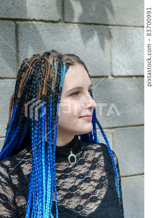 Young woman against gray stone wall. Lovely woman with long blue pigtails. Daytime. Selective Focus 83700991