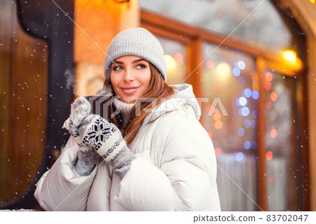 Smiling beautiful girl stands outside while holds coffe to go in hands. Festive mood. Christmas time Smiling beautiful girl stands outside while holds coffe to go in hands. Festive mood. Christmas time 83702047