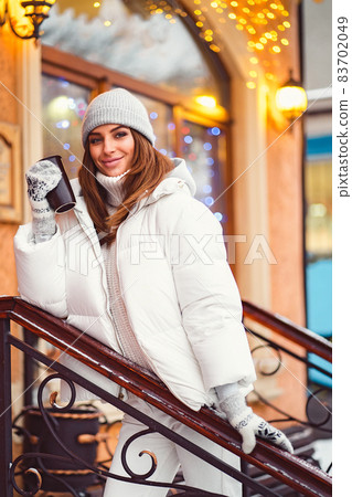 Smiling girl stands on stairs outside while holds coffe to go in hand. Festive mood. Christmas time Smiling girl stands on stairs outside while holds coffe to go in hand. Festive mood. Christmas time 83702049