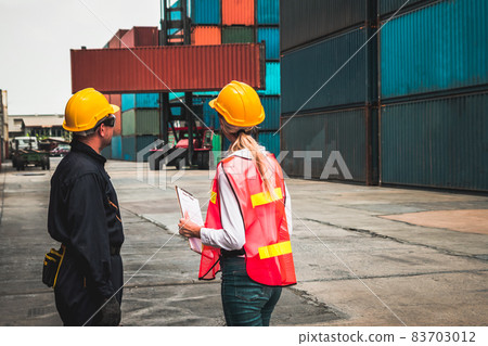 Industrial worker works with co-worker at overseas shipping container yard Industrial worker works with co-worker at overseas shipping container yard 83703012
