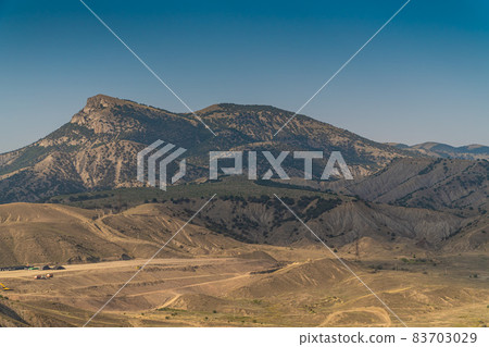 The Republic of Crimea. July 18, 2021. Picturesque landscape of the Crimean mountains near the city of Sudak in warm sunny weather. The Republic of Crimea. July 18, 2021. Picturesque landscape of the Crimean mountains near the city of Sudak in warm sunny weather. 83703029