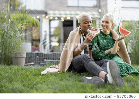 Multiracial couple eat watermelon in their garden 83703066