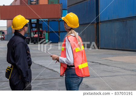 Industrial worker works with co-worker at overseas shipping container yard Industrial worker works with co-worker at overseas shipping container yard 83703191