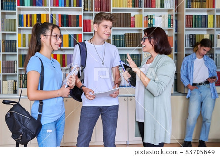 A group of teenage students in the library talking with a female teacher. A group of teenage students in the library talking with a female teacher. 83705649