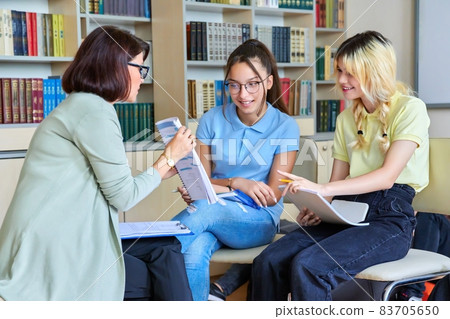 Female teacher working with teenage students in the library. 83705650