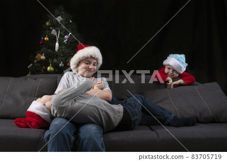 Three children in Santa hats are playing on sofa with Christmas tree in the background. Three children in Santa hats are playing on sofa with Christmas tree in the background. 83705719