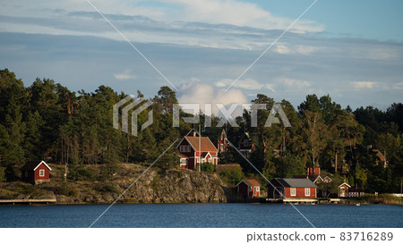 Beautiful Red Swedish Wooden Log Cabin Houses On Rocky Island Coast In Summer with forest Beautiful Red Swedish Wooden Log Cabin Houses On Rocky Island Coast In Summer with forest 83716289