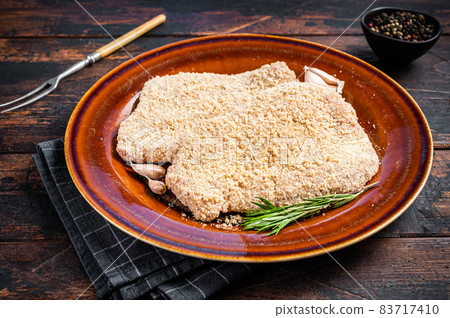 Raw Breaded German Wiener schnitzel on a rustic plate with herbs. Dark wooden background. Top view 83717410
