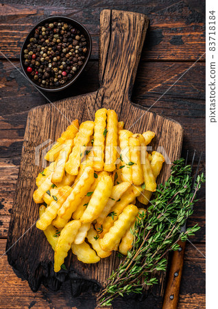 Baked Crinkle French fries potatoes sticks or chips on a wooden board. Dark wooden background. Top view Baked Crinkle French fries potatoes sticks or chips on a wooden board. Dark wooden background. Top view 83718184