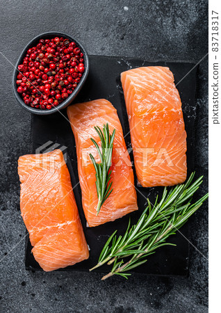 Raw salmon fillet steaks on marble board with herbs. Black background. Top view Raw salmon fillet steaks on marble board with herbs. Black background. Top view 83718317