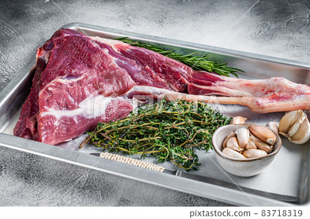 Uncooked Raw goat or lamb leg with herbs in baking tray. White background. Top view Uncooked Raw goat or lamb leg with herbs in baking tray. White background. Top view 83718319