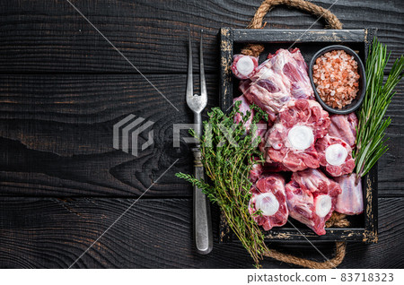 Raw veal beef Oxtail Meat in wooden tray with thyme. Black wooden background. Top view. Copy space Raw veal beef Oxtail Meat in wooden tray with thyme. Black wooden background. Top view. Copy space 83718323