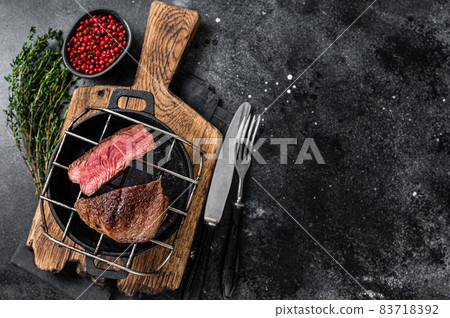 Beef tenderloin steak is grilled on a grill pan. Black background. Top view. Copy space 83718392